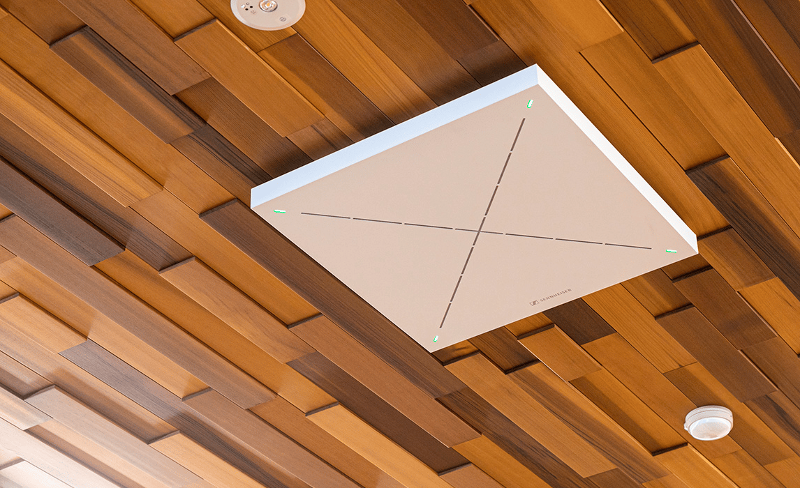 Sennheiser ceiling microphone mounted on a wooden panel ceiling.