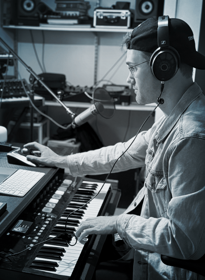 Musician wearing Sennheiser headphones working on a keyboard in a recording studio.
