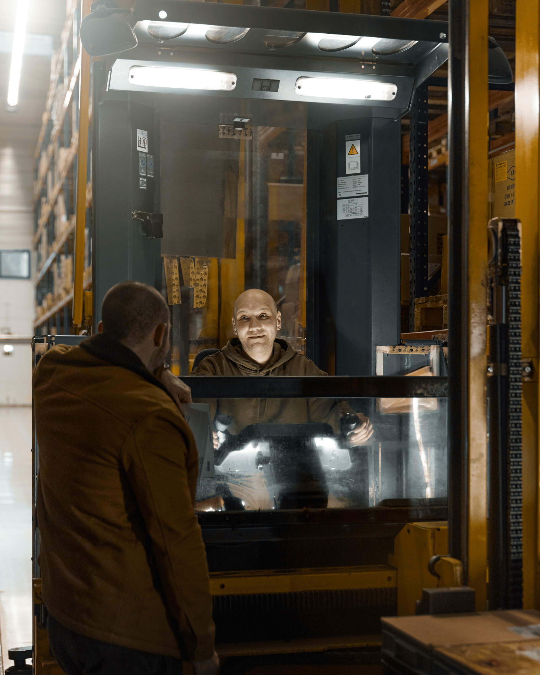 Warehouse worker operating a forklift while another person observes.