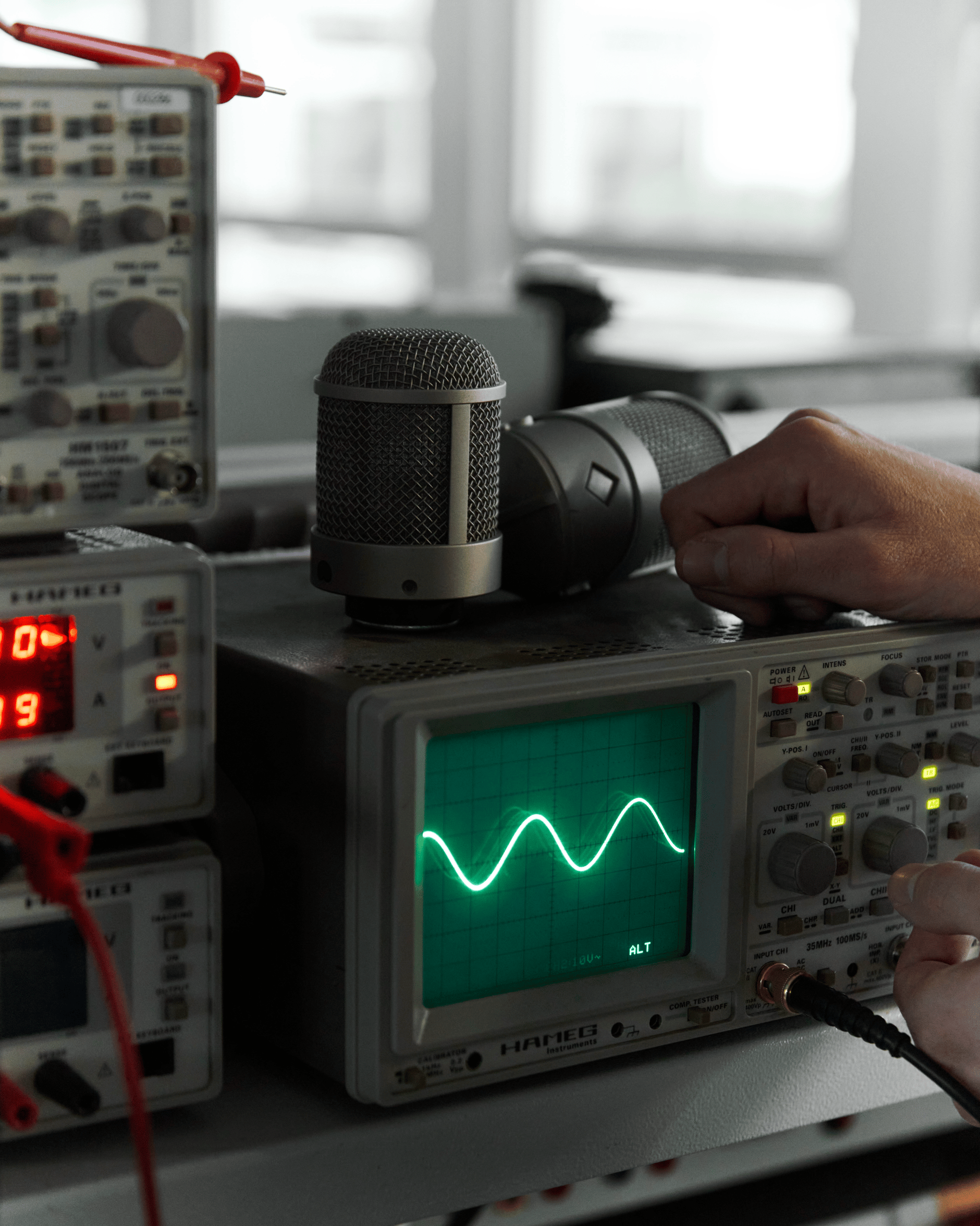 Person adjusting audio equipment with microphone and oscilloscope displaying waveform.