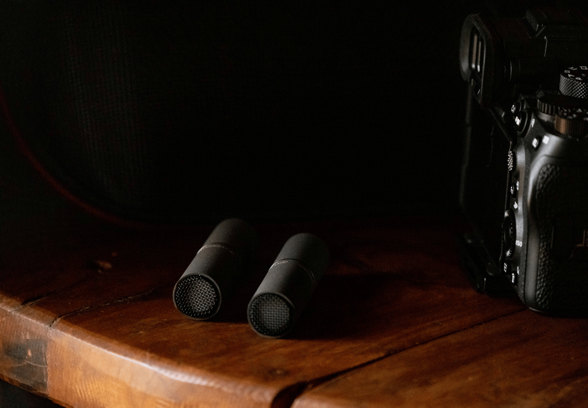Sennheiser MKH 8000 series microphones on a wooden surface next to a camera.