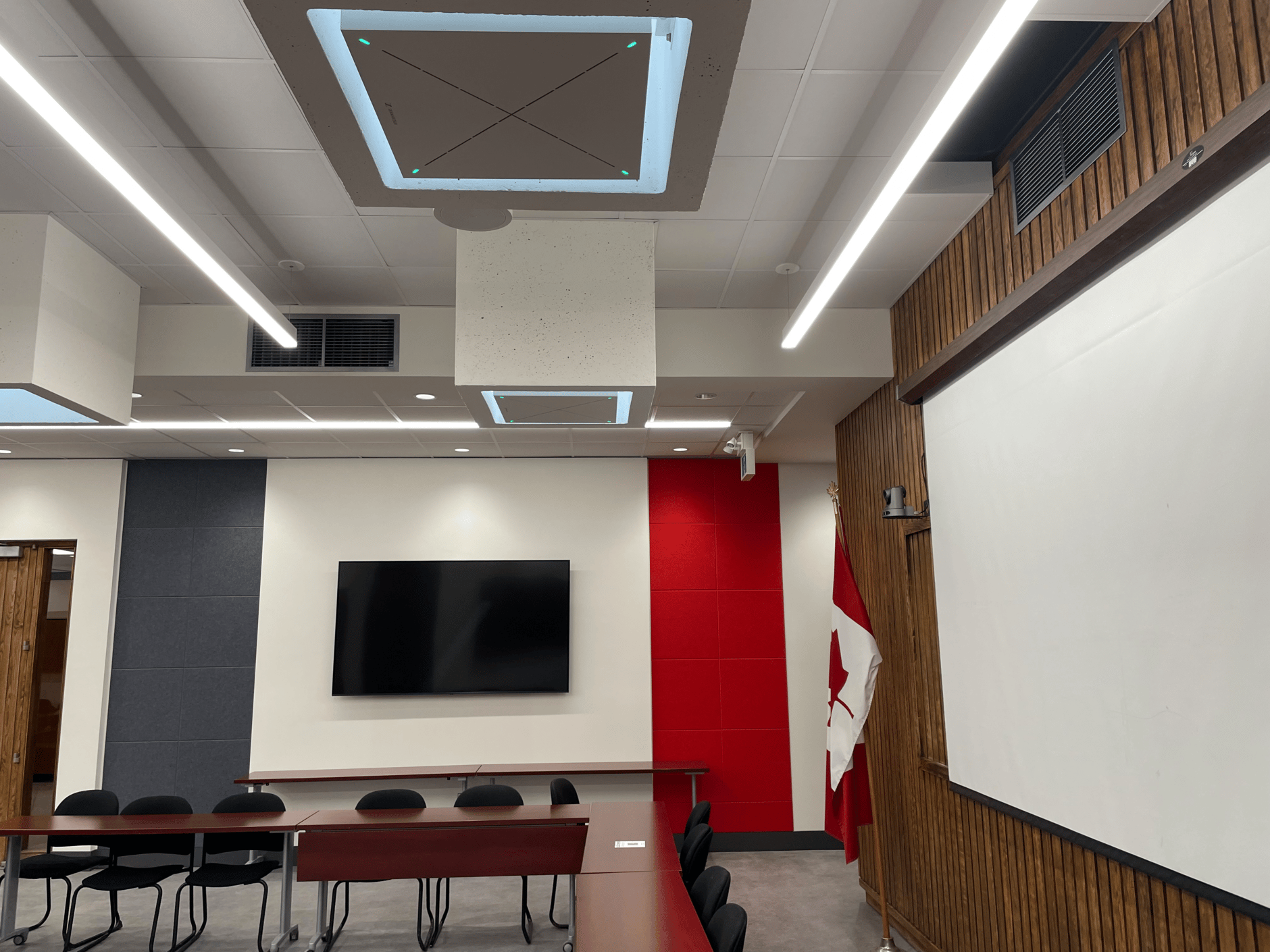 Modern conference room with a large screen, Canadian flag, and ceiling-mounted acoustic panels.