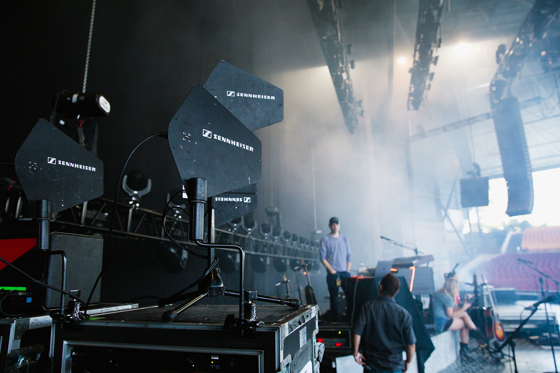 Big black Loudspeakers standing on a case in a concert hall with a handfull of people being in the background