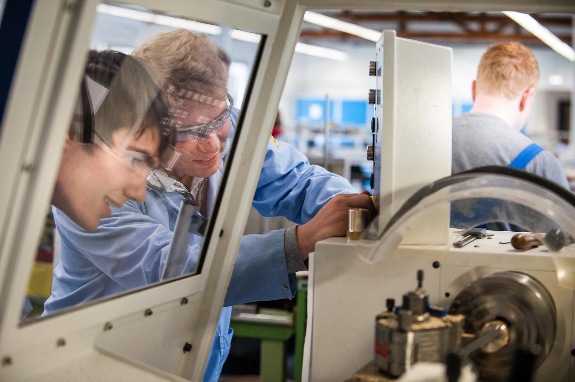 Two Men working in the production with safety glasses stand in front of a machine and turn switches