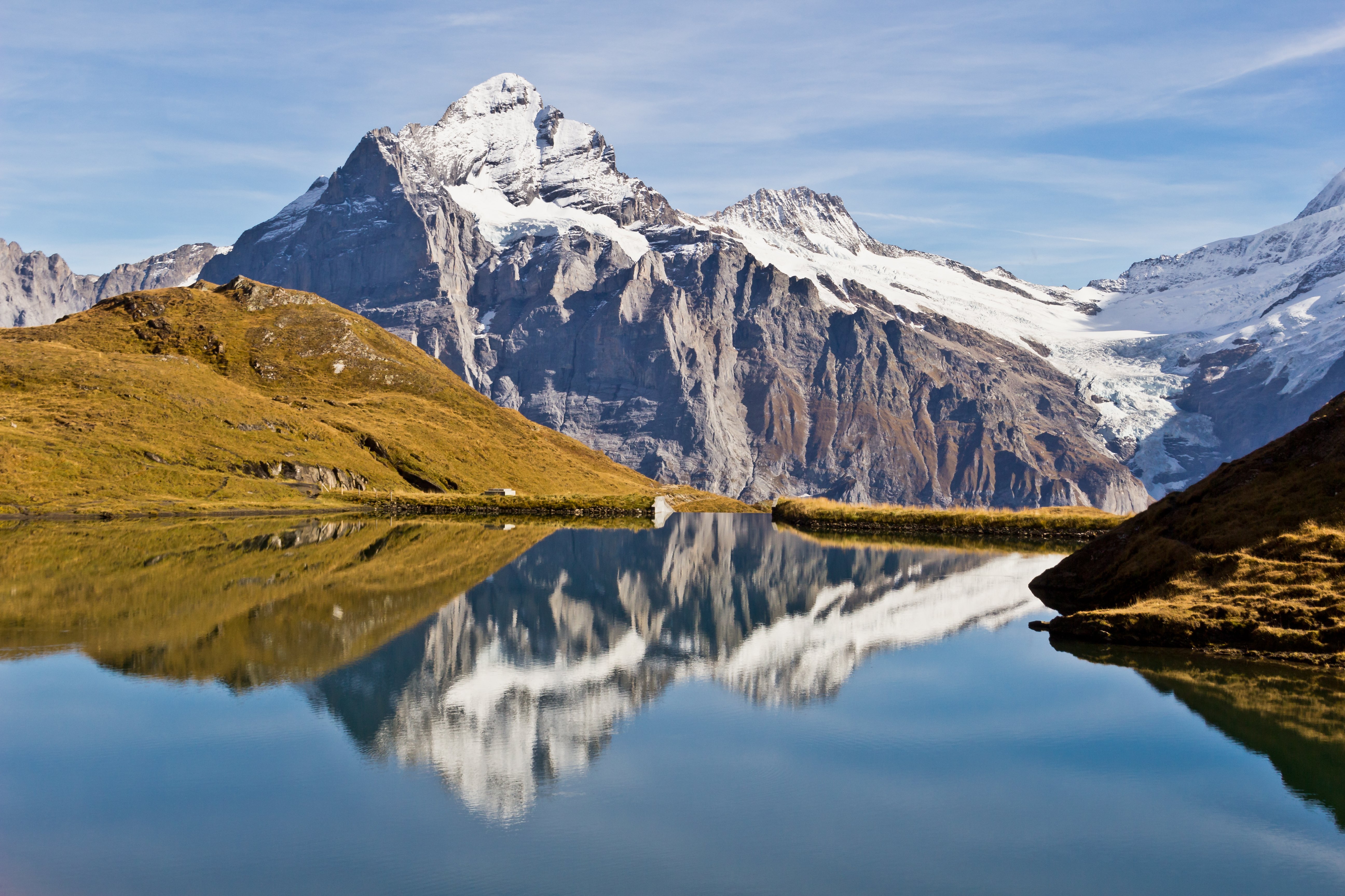 Snow-capped mountains reflecting in a clear lake under a blue sky.
