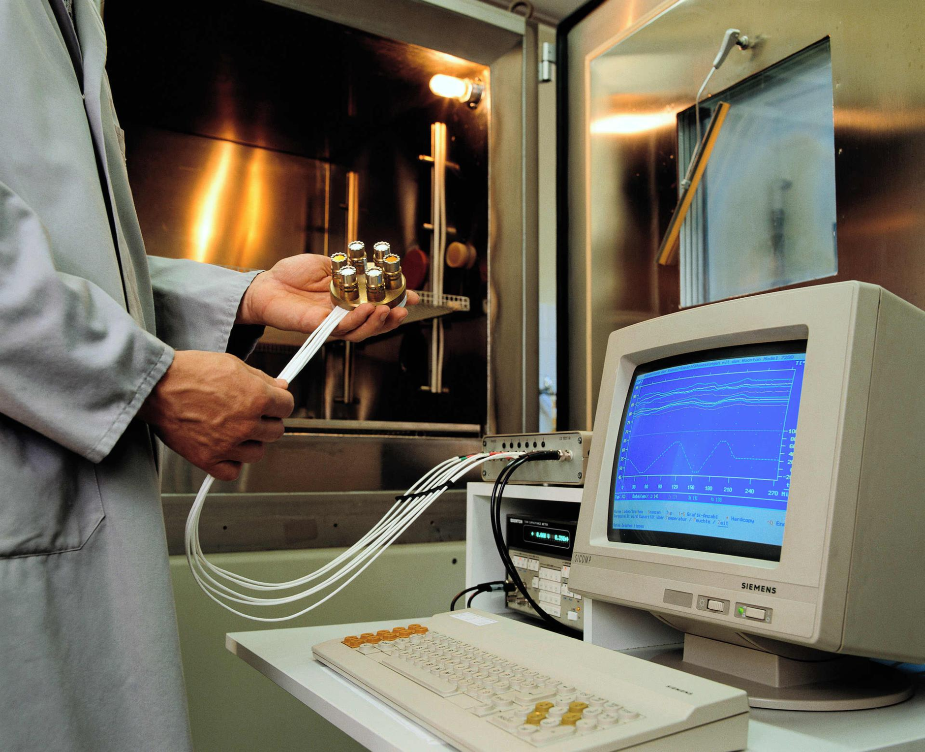 A person with some kind of technical device, which is connected to various cables is standing in front of an old Computer