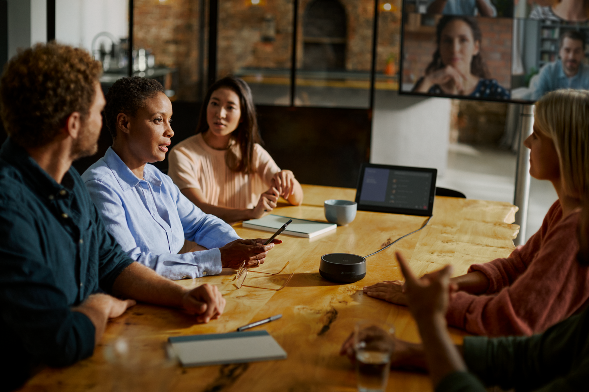 A group of collegues from different nationalities sitting around a table having a meeting with a speaker in the middle 