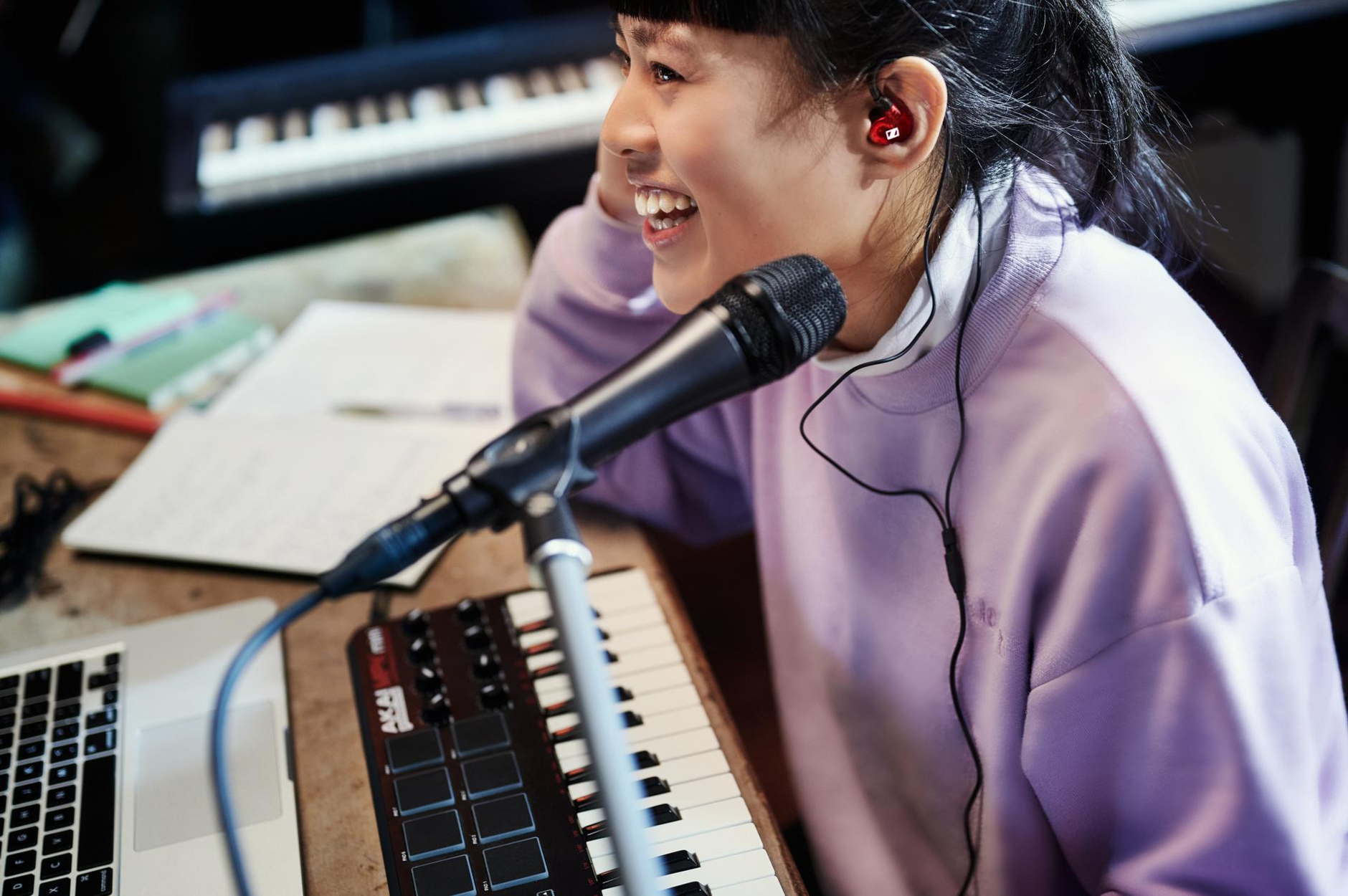 Asian woman sitting smiling in a music studio in front of her equipment