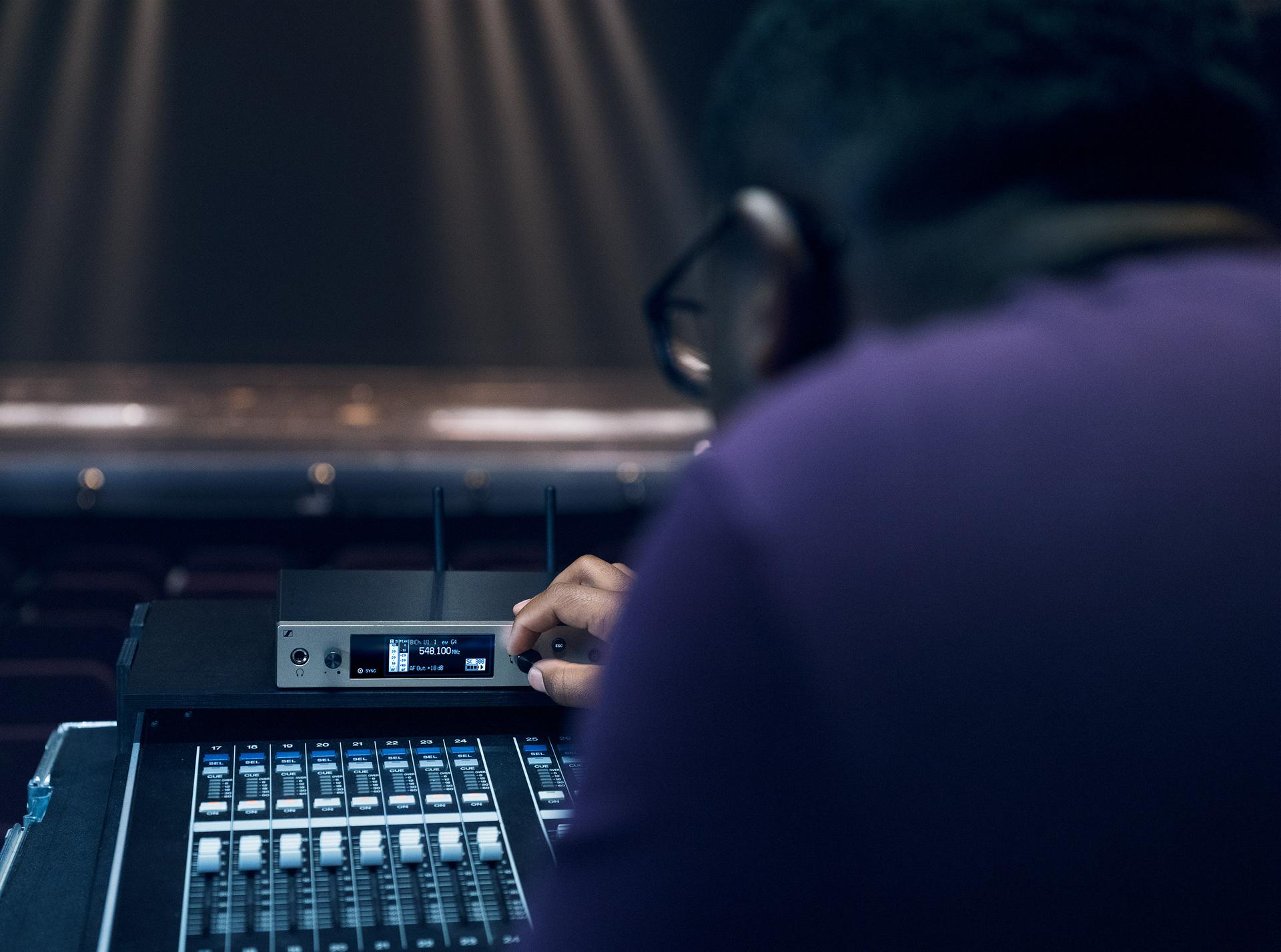 Sound engineer adjusting Sennheiser wireless microphone system on a mixing console during a live performance.