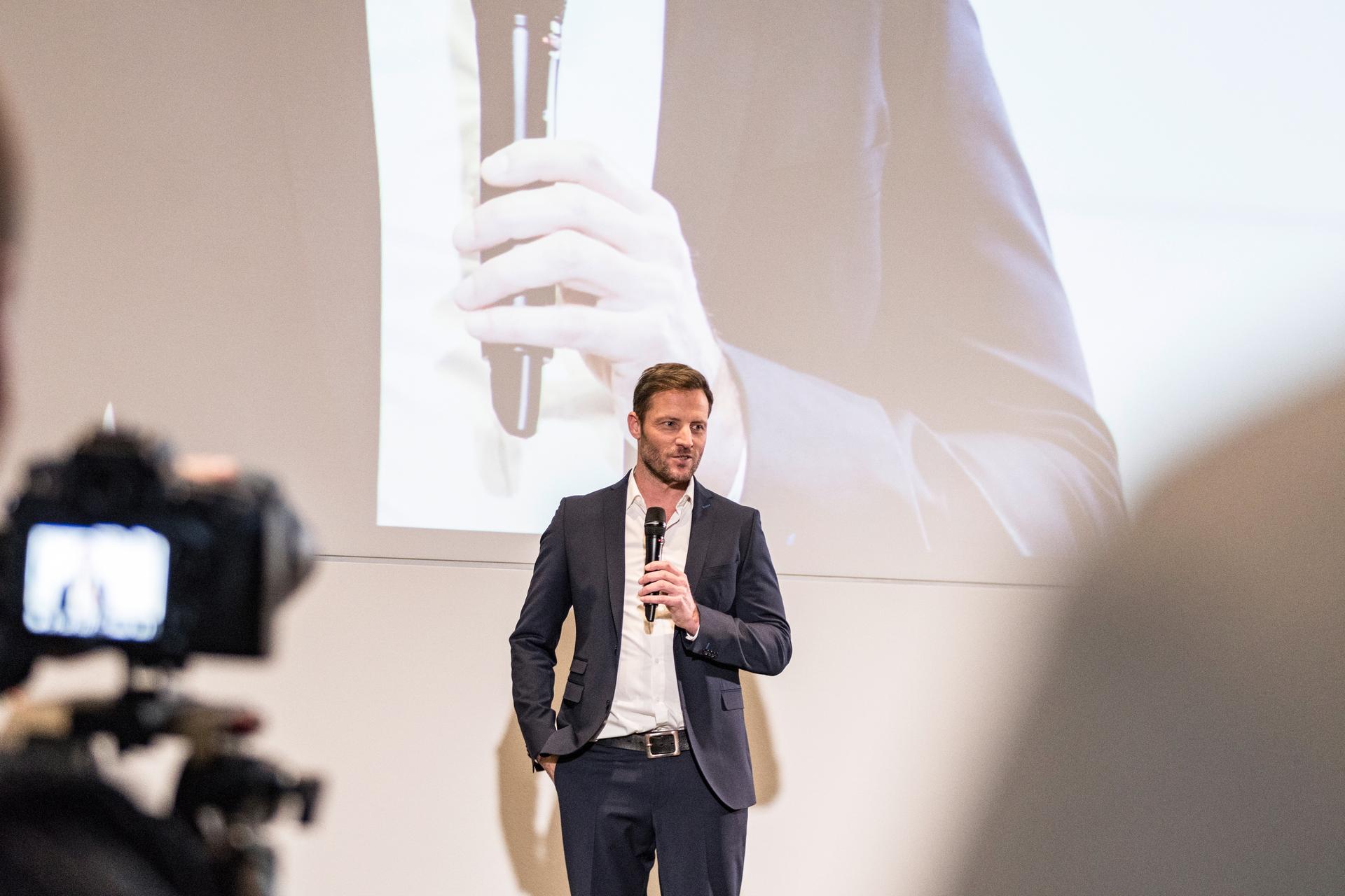 Man in a suit holding a microphone giving a presentation.