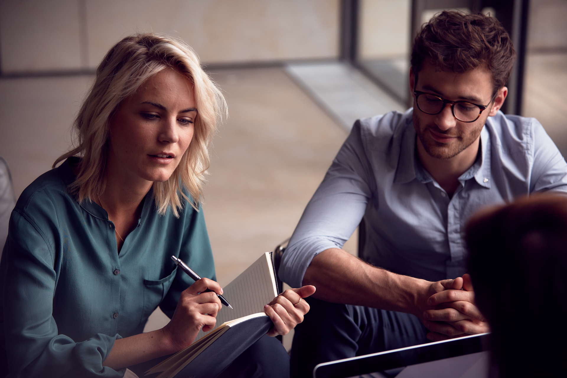 Two colleagues discussing and taking notes in a meeting.