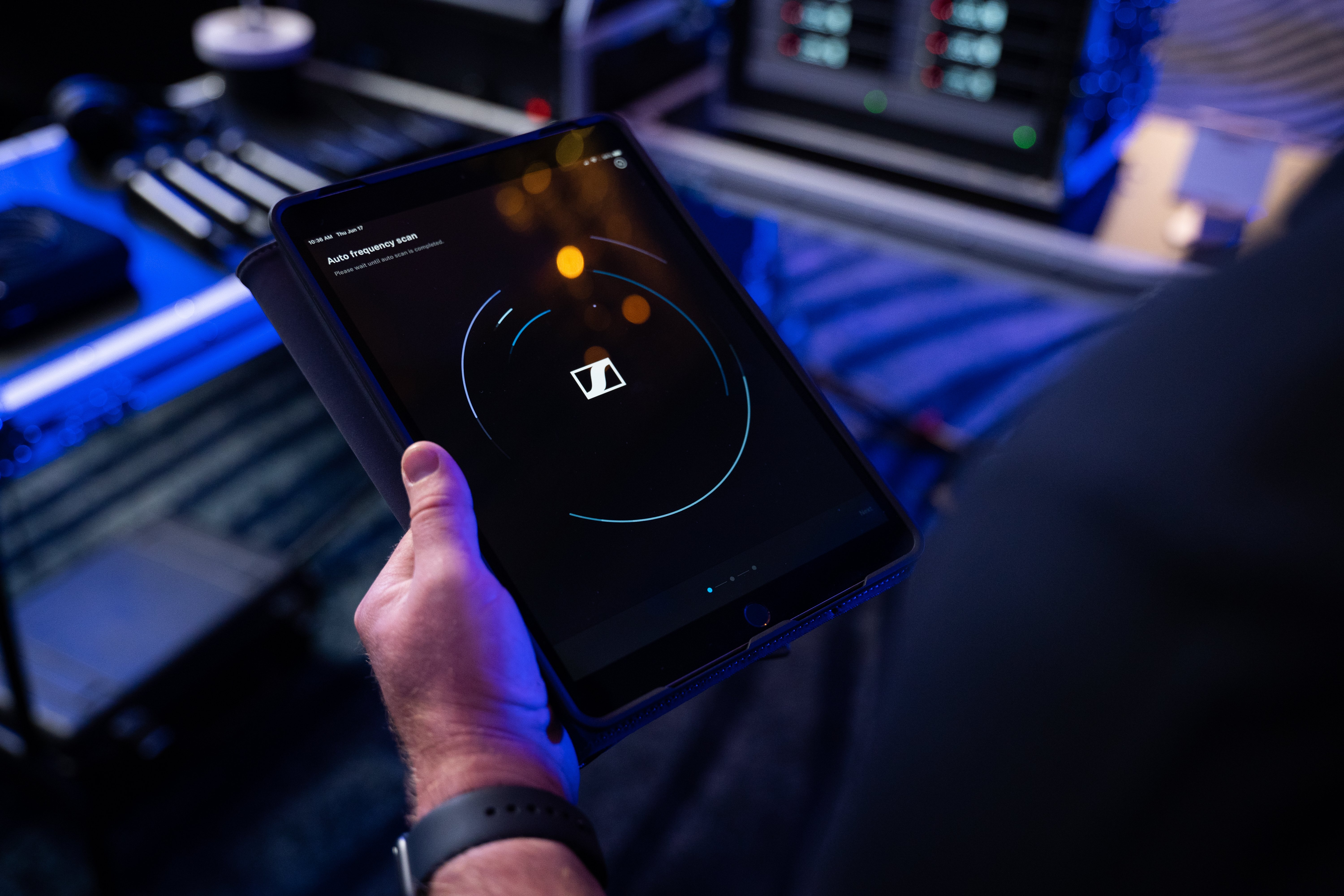 Person holding a tablet displaying Sennheiser audio control interface in a professional audio setup.