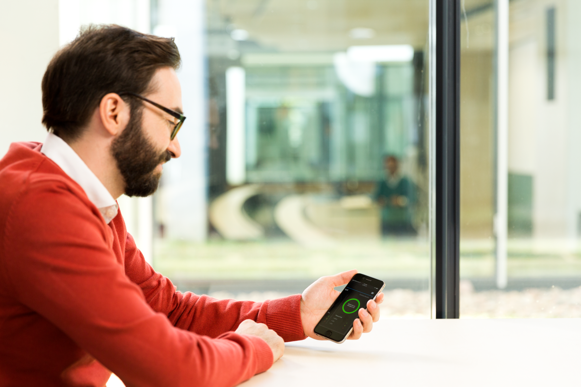 Man using Sennheiser mobile app on smartphone in modern office.