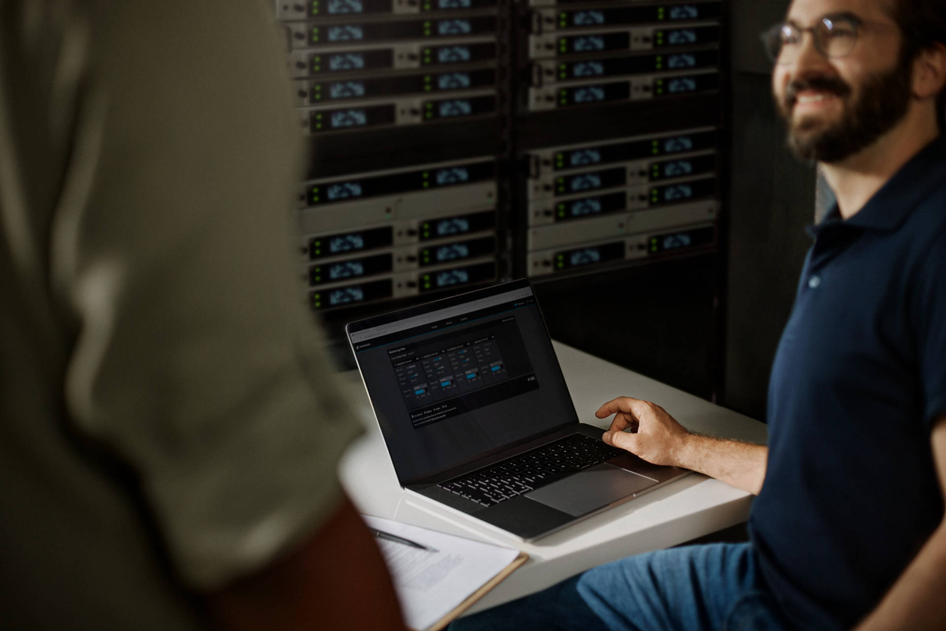 Man using laptop to configure Sennheiser audio equipment in server room.
