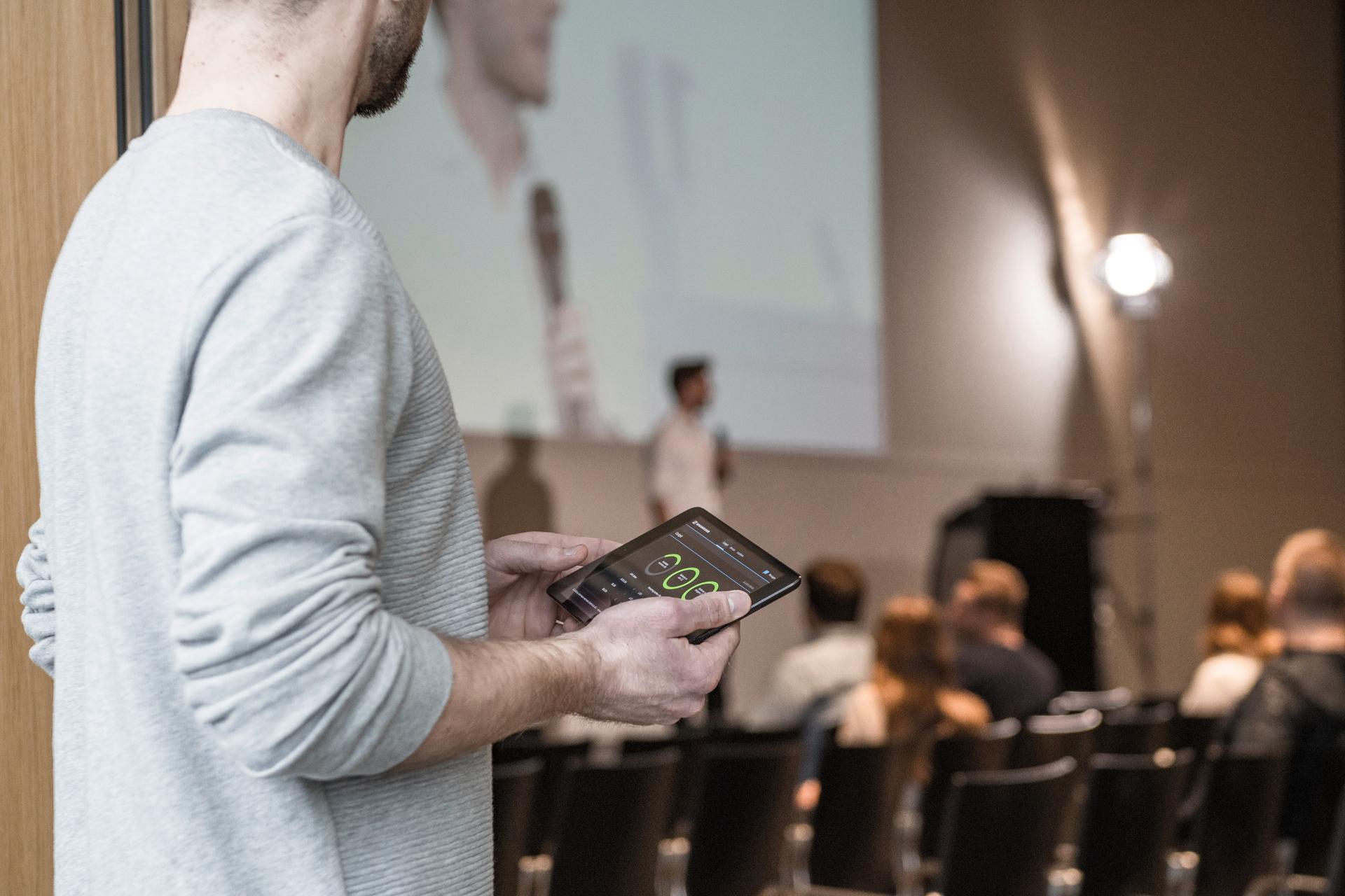 Person using a tablet to control audio settings during a presentation.