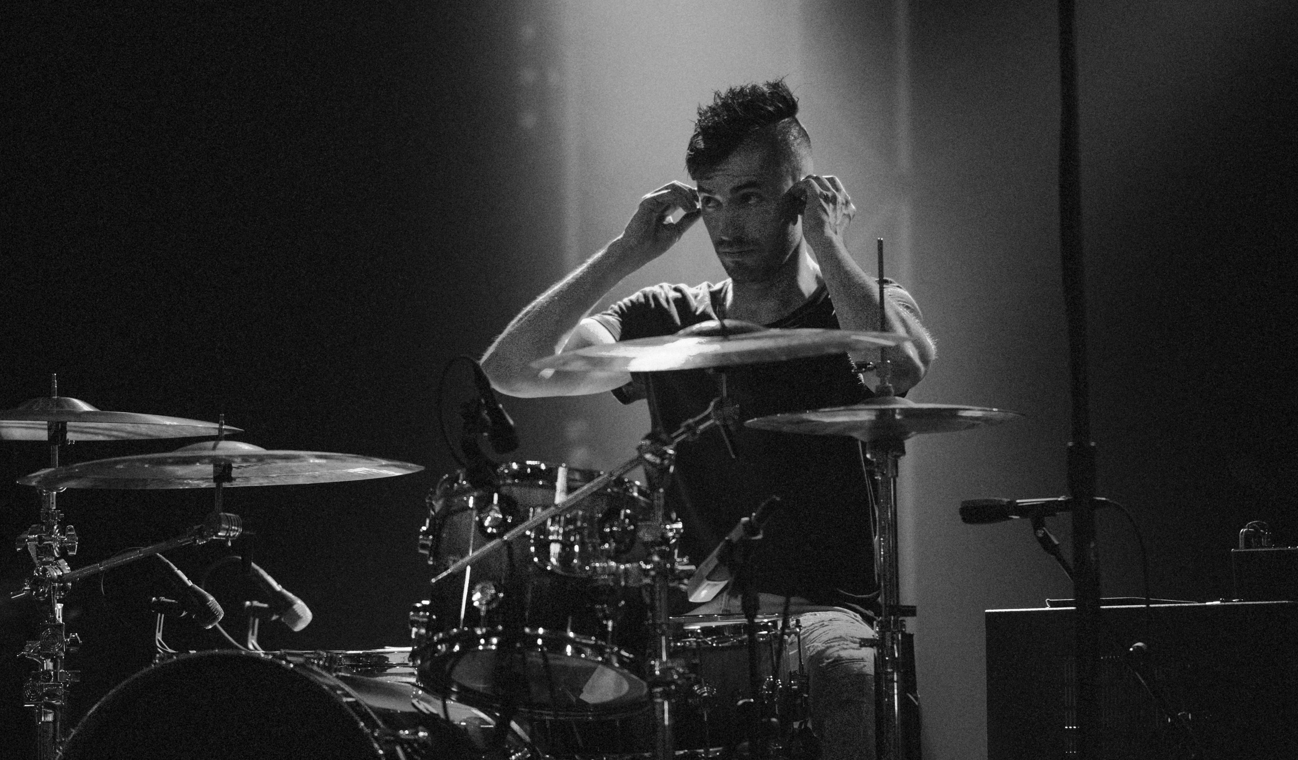 Drummer adjusting headphones while playing drums on stage.