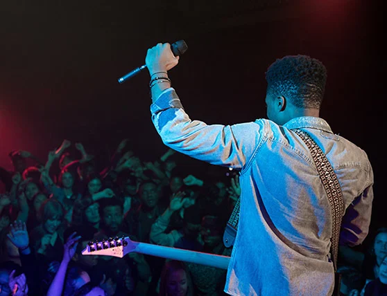 Musician performing on stage with a guitar and microphone in front of an audience.